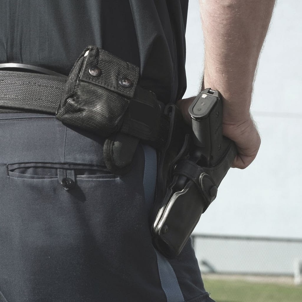 This is a closeup image of a security guard standing outside. The image focuses on his belt and holster. His hand is on his gun. This image is used in the BPS Security Article titled, “When is it Okay for a Security Guard to Draw Their Gun?”