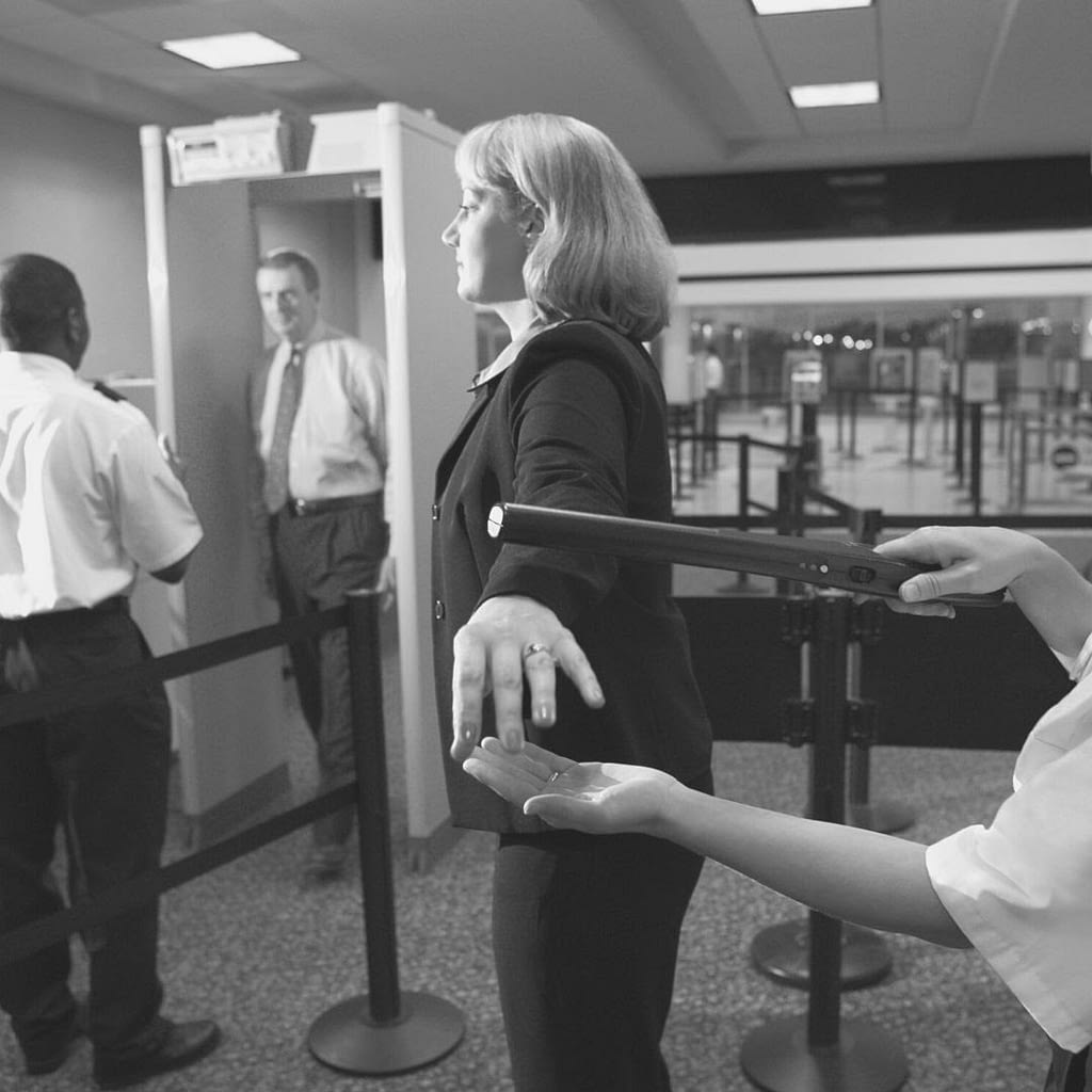 Women going through a security checkpoint. She is now past the metal detectors and is getting wand down. This image is used to show security guards can do and cannot do.