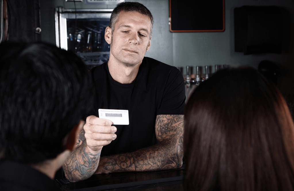 This image shows a bouncer at a club/bar checking two individuals’ IDs prior to entry. This image is used in the BPS Security article titled, “How to be a Great Private Security Guard: De-escalation Tactics for Venues Serving Alcohol ”.