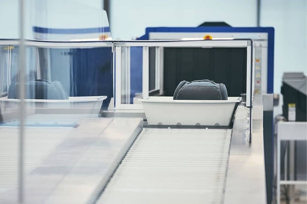 This image shows the airport security machine that scans bag, and is showing a bag, in a tray, exiting the scanning machine. This image is used in the BPS Security article titled, “How does the recent ‘no mask’ policy affect airport security?”
