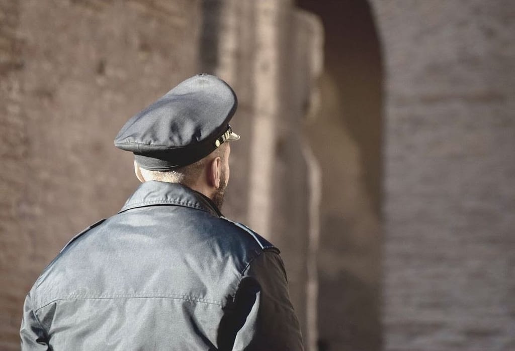 This is an image of a security guard, facing a building. The guard is in focus, and we see his back, while the building is out of focus. This image is used in the BPS Securit article titled, “How Offering Benefits to Security Guards Can Help Fix the Broken Security Industry”