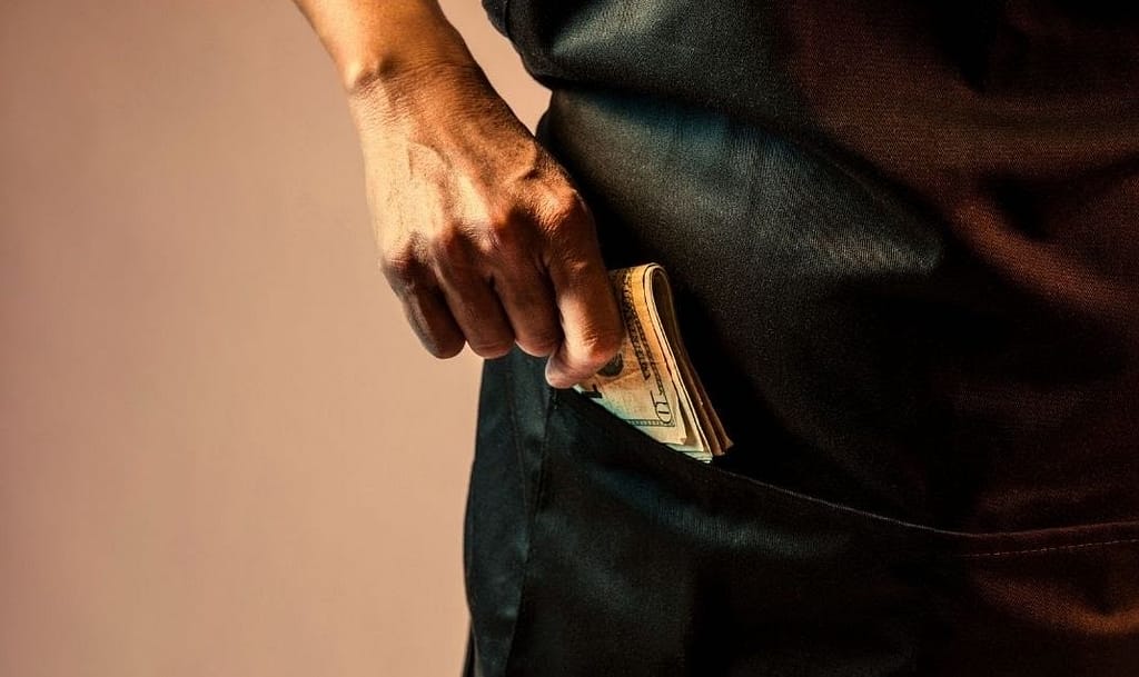 This photo is of a man shoving a wod of cash into their jean pocket. This image is used in the BPS Security article titled, “How Company Culture Affects Security”.