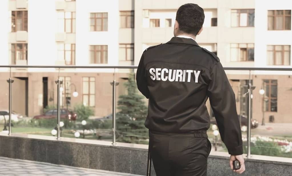 This is an image of a security guard (we see his back) standing and looking towards some buildings. This image is used in the BPS Security article titled, “Do you know the difference between private and public security?”