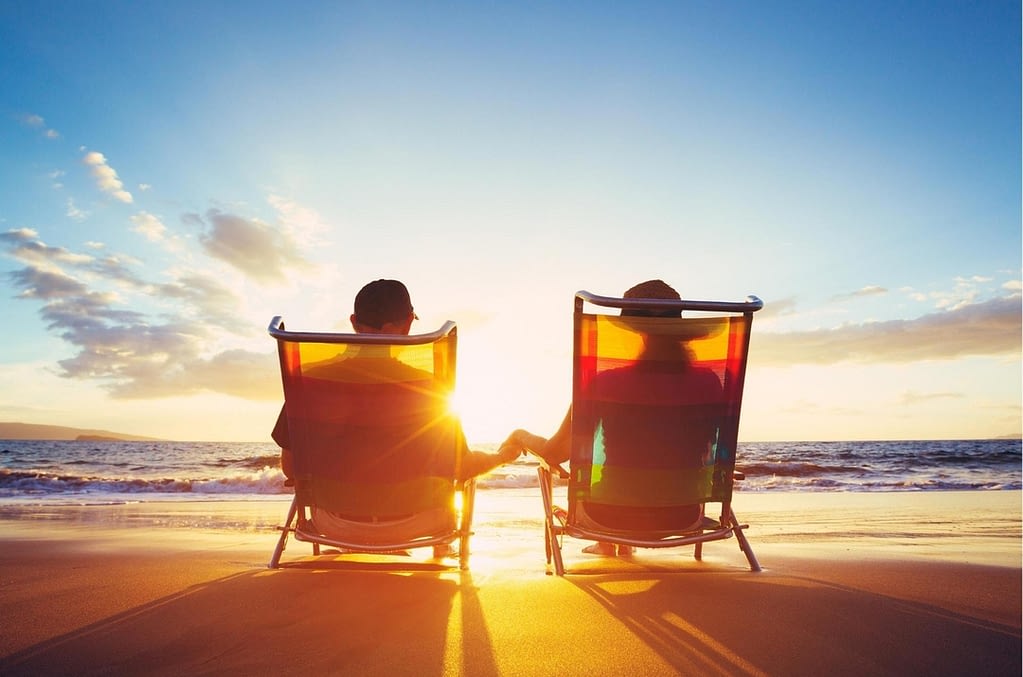 This is an image of two people sitting in lawn chairs on the beach, watching the sun go down over the ocean. This image is used in the BPS Security article titled, “Top 5 Tips to Secure Your Home While On Summer Vacation”.