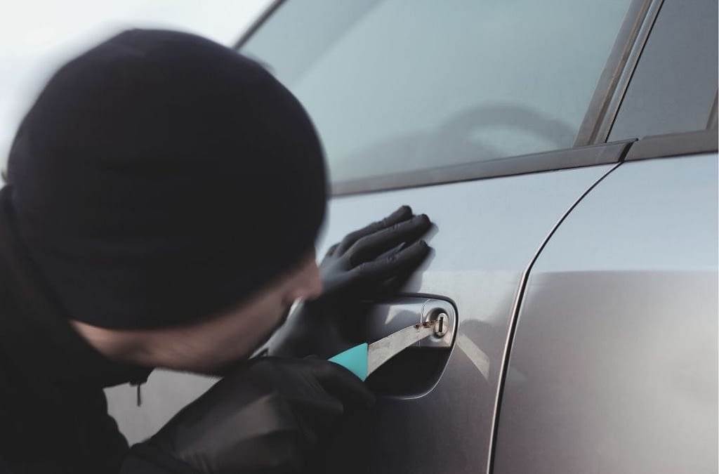 This image shows a thief picking a car’s lock in broad daylight. This image is used in the BPS Securit article titled, “How to Prevent Vehicle Theft”.