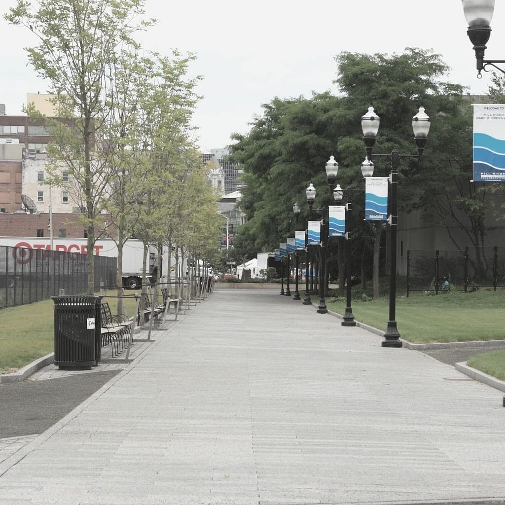 Image of a walkway in between building with trees lining one side and lamps lining the other side. This image is use for the BPS Security Blog How Environmental Design Can Reduce Crime