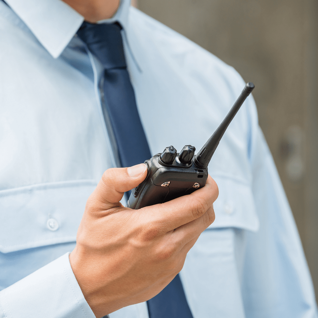 this is a closeup image of a uniformed security guard holding a walkie talkie. This image is used in the BPS Security Blog titled, “The Importance of Communication in the Security Industry”