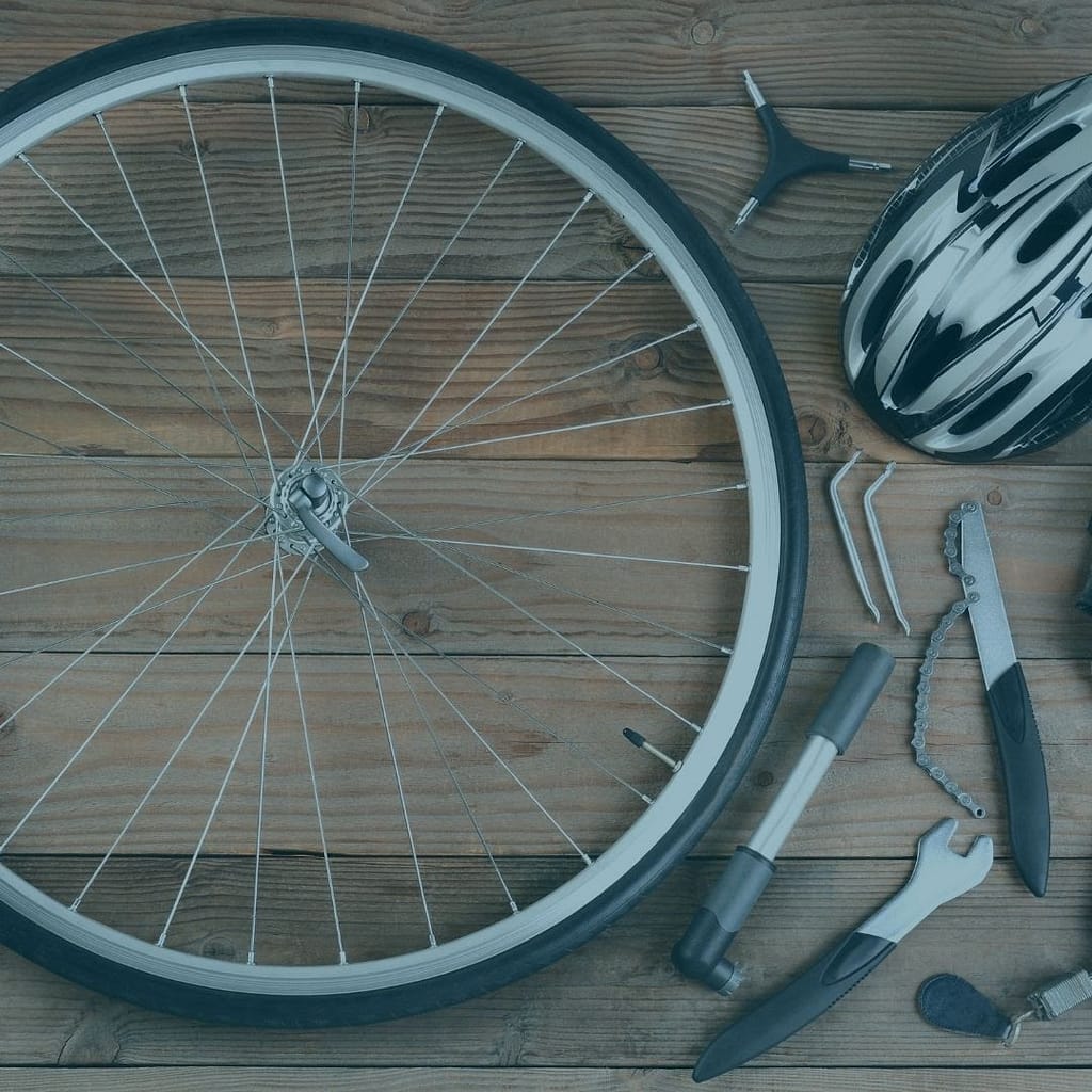 This is a top down picture of a bicycle wheel, laying on a wooden floor, with a helmet and bicycle tools placed next to the wheel. This image is used in the BPS Security Blog post titled “Is There Room for Lazy Security Guards Within the Security Industry?”.