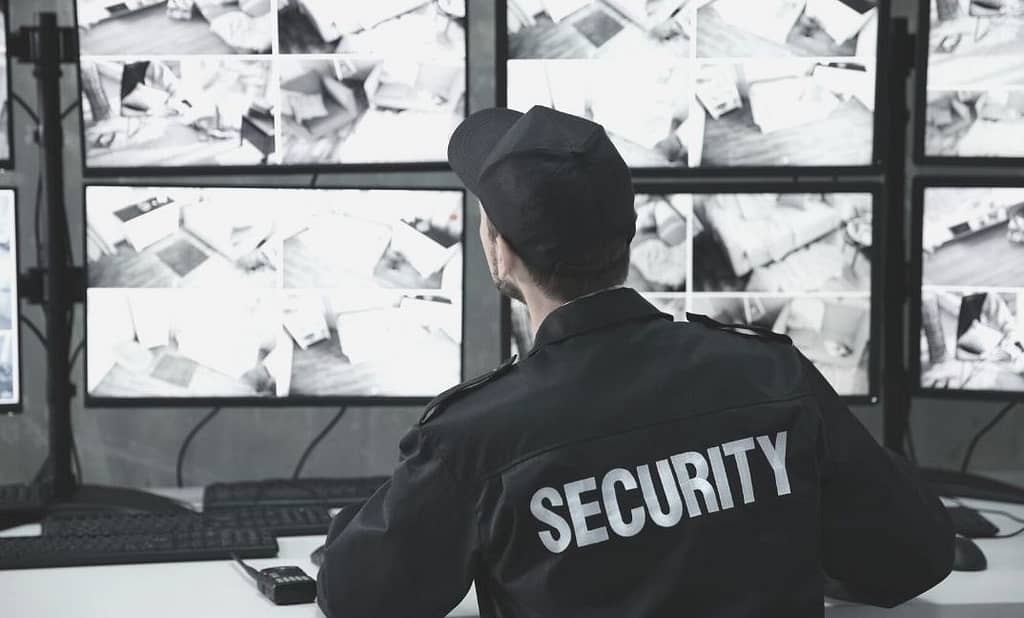 This is an image of a security guard (we see his back) sitting at a desk, looking at eight screens showing security footage. This image is used in the BPS Security article titled, “Do you know the difference between private and public security?”