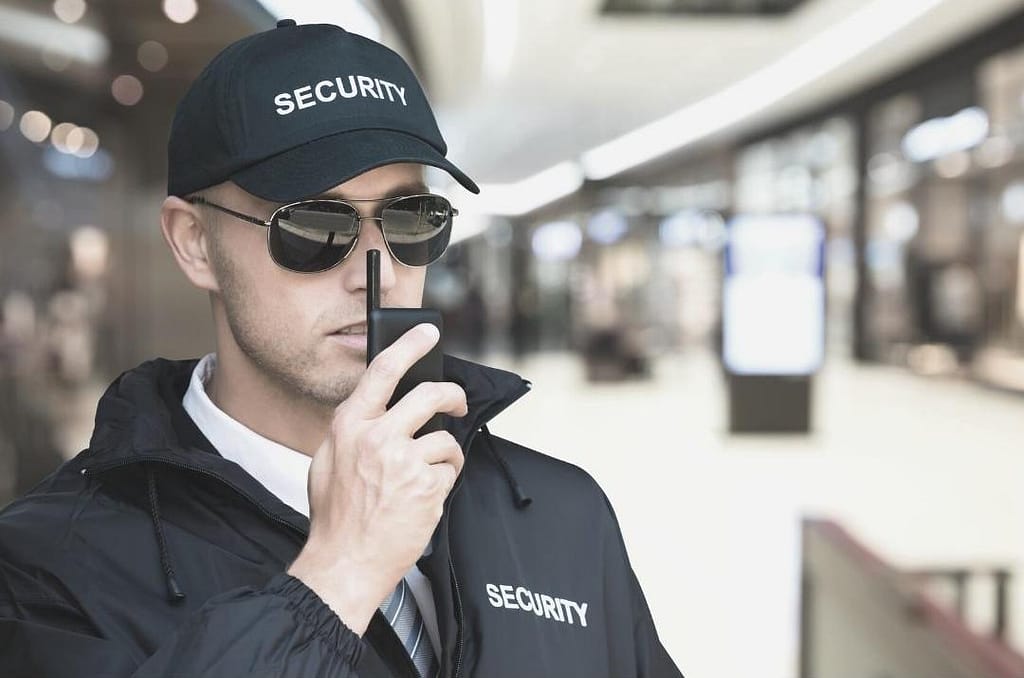 This is an image of a security guard standing near a metro station, holding a walkie talkie up to this mouth, about to talk. This image is used in the BPS Security article titled, “5 Items Security Guards Carry to Keep You Safe”.