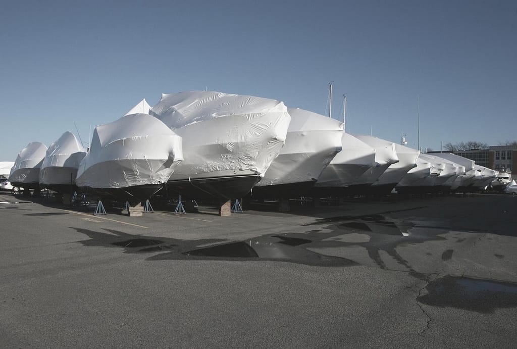 This is an image of multiple boats lifted and sitting in an outdoor, off-site storage unit. All of the boats are covered with a protective fabric cover. This image is used in the BPS Security article titled, “Keep Your RVs and Boats Safe at Off-Site Storage”.