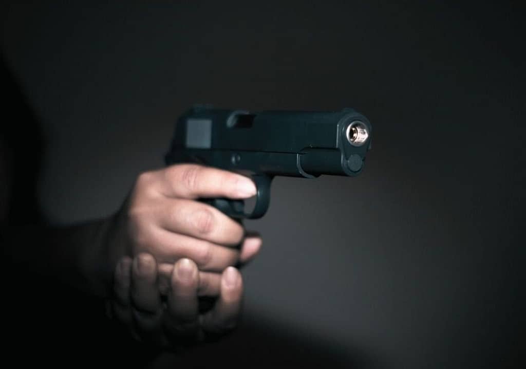 This is an image of a hand holding a gun in front of a black wall. This image is used in the BPS Security article titled, “Can a Surveillance System Create a Middle Ground in the Gun Debate?”